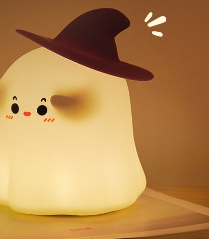 Ghost silicone night light wearing a witch hat, glowing warm on a book