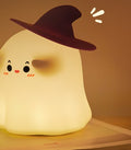 Ghost silicone night light wearing a witch hat, glowing warm on a book