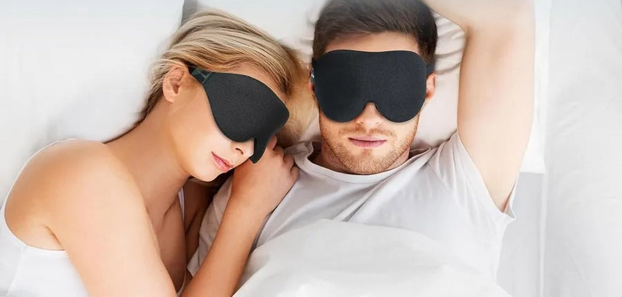 A couple asleep in bed, both wearing the contoured 3D sleep mask